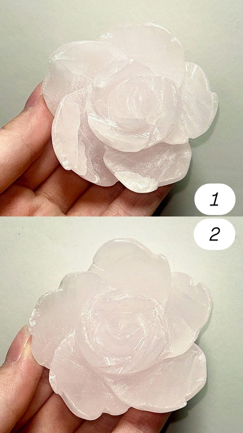 May include: A carved rose made of pale pink stone. The flower has multiple layers of petals, with a detailed texture. The rose is a light pink color and appears to be smooth. The image is taken from two different angles.