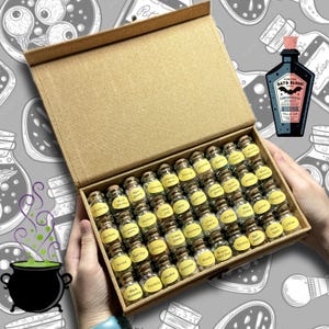 May include: A box of small glass bottles with cork stoppers, each labeled with a different name. The box is open, revealing the contents, and is held by hands. A bottle of "Bats Blood" is in the background.