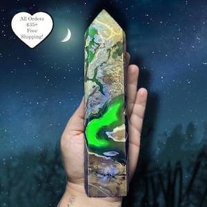 May include: A tall, rectangular crystal obelisk with a pointed top. The obelisk features a mix of colors, including green, gold, and brown, with a glowing green section. The background is a dark blue with a crescent moon and stars.