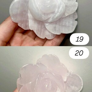 May include: Two carved rose sculptures. The top rose is a pale white, and the bottom rose is a soft pink. The petals are detailed and textured, with a natural, stone-like appearance. The background is a neutral gray.