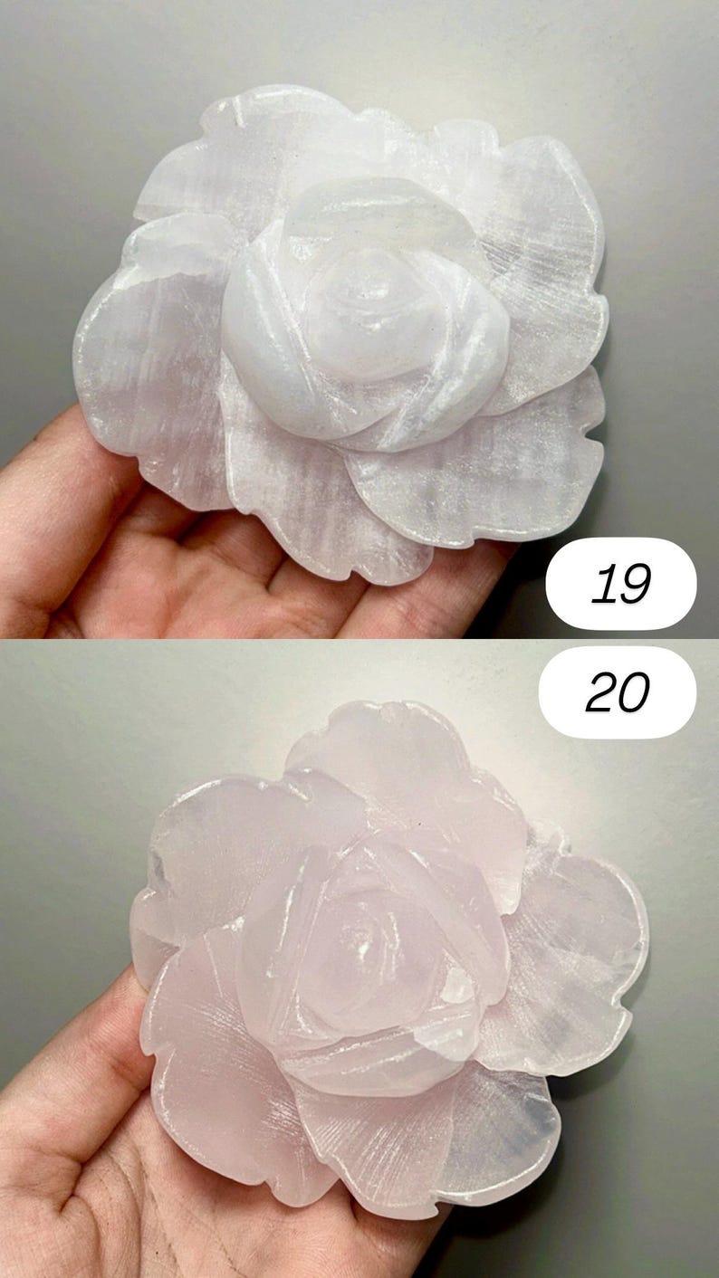 May include: Two carved rose sculptures. The top rose is a pale white, and the bottom rose is a soft pink. The petals are detailed and textured, with a natural, stone-like appearance. The background is a neutral gray.