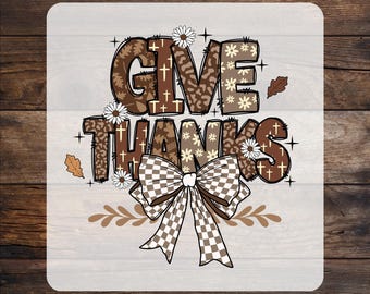 May include: A custom DTF transfer featuring the text GIVE THANKS in brown and beige patterns including leopard print, crosses, and flowers. The design is accented with small white daisies, brown oak leaves, and a large checkered bow at the bottom.