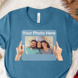 May include: A blue t-shirt with a white frame that says "Your Photo Here" and a photo of a family of three inside the frame.