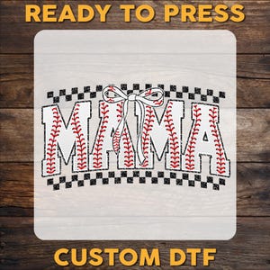 May include: A white iron-on transfer design with the word "MAMA" in black letters with a baseball stitch pattern. A red bow is above the word. The design is on a checkered background.