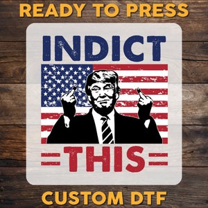 May include: A white square sticker with the text "INDICT THIS" in red and blue letters. The sticker features a black and white image of a man with a serious expression, giving the middle finger with both hands. The man is in front of an American flag with red and white stripes and blue stars. The text "READY TO PRESS" is in yellow letters at the top of the sticker and "CUSTOM DTF" is in yellow letters at the bottom.