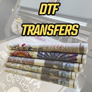 Pu&ograve; includere: Una pila di trasferimenti DTF colorati con il testo "DTF TRANSFERS" in lettere gialle su sfondo nero. I trasferimenti sono stampati su vinile trasparente e presentano vari disegni, tra cui un gallo, un sole e una citt&agrave;.