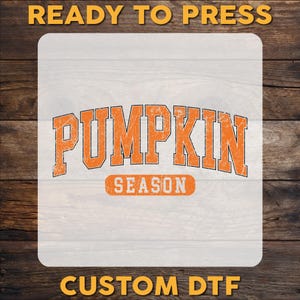 May include: A square DTF transfer sheet featuring the orange text PUMPKIN SEASON in a distressed collegiate font. The word PUMPKIN is arched above the word SEASON, which is enclosed in an orange rectangular border. The text READY TO PRESS and CUSTOM DTF appear in yellow at the top and bottom.