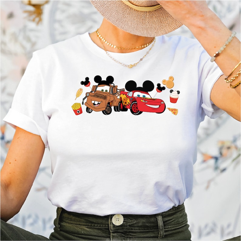 Pu&ograve; includere: Maglietta bianca con una grafica di Mater e Saetta McQueen di Cars, con orecchie di Topolino e icone di cibo Disney.