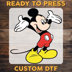 May include: A cartoon image of Mickey Mouse in a dynamic pose, wearing red shorts, yellow shoes, and white gloves. The image is set against a light gray background with the text "READY TO PRESS" at the top and "CUSTOM DTF" at the bottom.