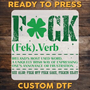 May include: A white rectangular design with the word "F*CK" in green, featuring a shamrock. Below, it reads "(Fek).Verb" and "IRELAND'S MOST USED WORD." Additional text explains its use in expressing annoyance. The words "READY TO PRESS" and "CUSTOM DTF" are also present.