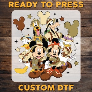May include: A digital transfer design featuring Mickey Mouse, Minnie Mouse, Donald Duck, Goofy, and Pluto dressed in safari outfits. The design includes stars and the text "READY TO PRESS CUSTOM DTF".