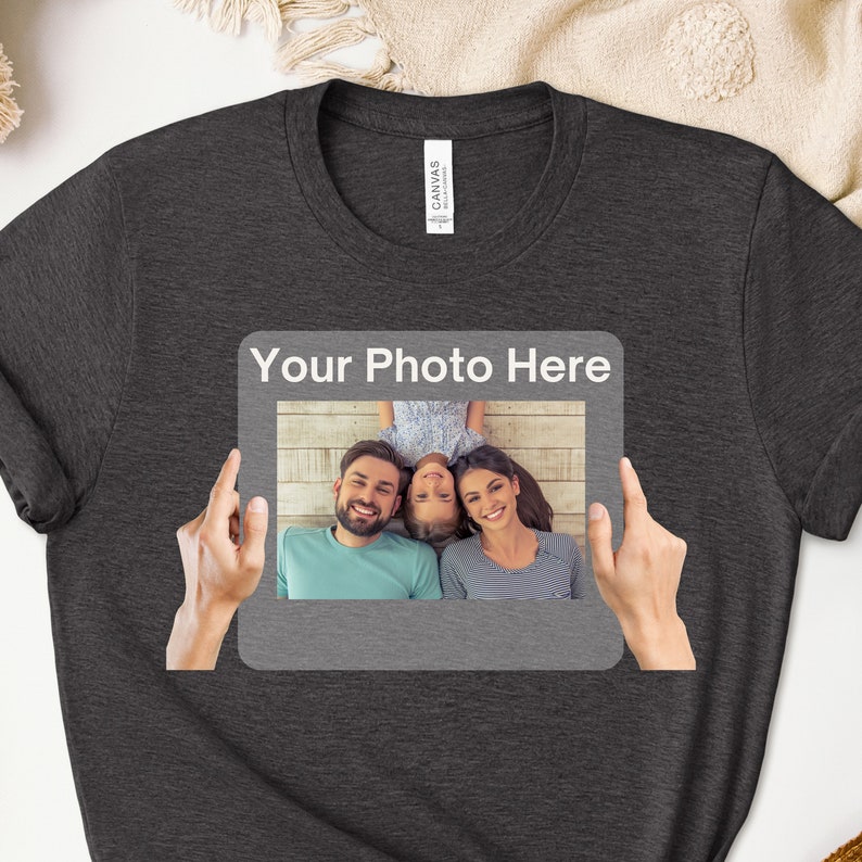 May include: A dark gray t-shirt with a white frame and the text "Your Photo Here" printed on the front. The frame contains a photo of a family of three, a man, a woman, and a child, smiling and lying on a wooden floor.