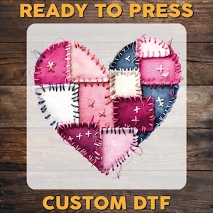 May include: A heart-shaped design composed of various fabric patches in shades of pink, blue, and white, stitched together with contrasting thread. The words "READY TO PRESS" and "CUSTOM DTF" are printed in a gold color.