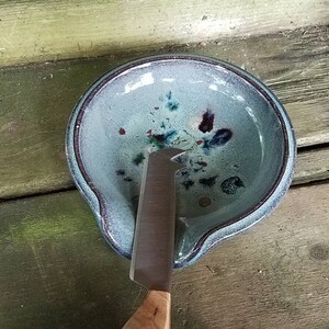Op de afbeelding: Een blauwe keramische botervloot met een mes erin. De vloot heeft een gespikkeld glazuur met blauwe, groene en rode accenten.