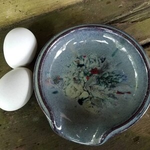 Op de afbeelding: Twee witte eieren naast een blauwe en witte keramische eier-vormige schaal met een bruine rand.