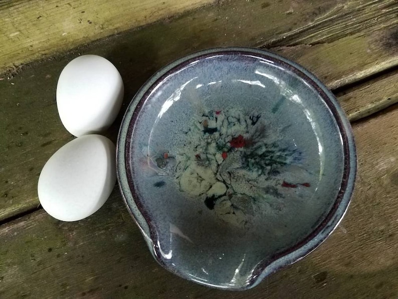 Op de afbeelding: Twee witte eieren naast een blauwe en witte keramische eier-vormige schaal met een bruine rand.