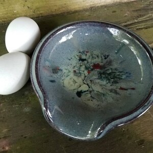 Op de afbeelding: Een blauwe en witte keramische mengkom met een gespikkelde glazuur en een donkerpaarse rand. De kom heeft een diepe, ronde vorm met een brede, platte basis en een klein tuitje aan de ene kant.