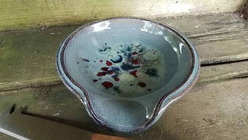Op de afbeelding: Een blauwe keramische lepelsteun met een gespikkeld glazuur in tinten blauw, wit en rood.
