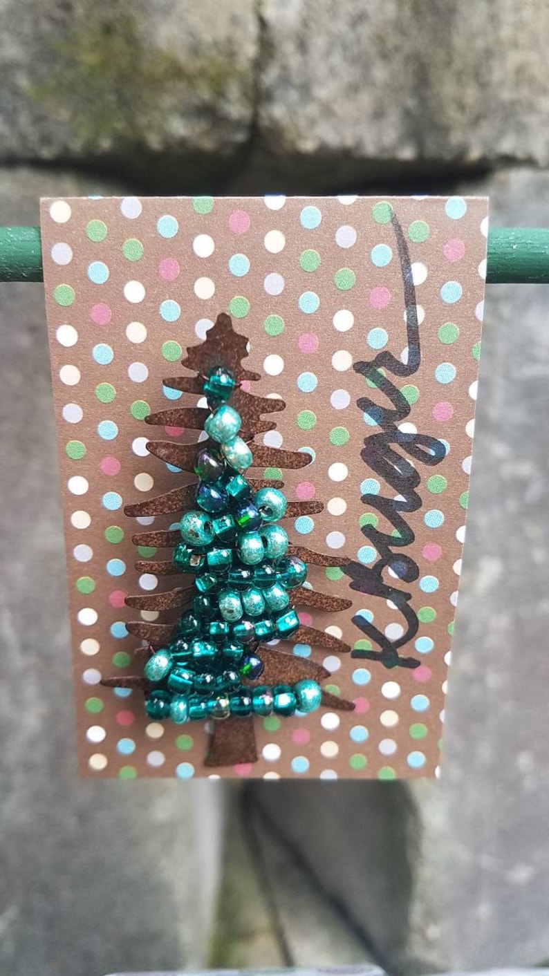 Puede incluir: Un adorno de &aacute;rbol de Navidad de cuentas azul turquesa sobre una tarjeta marr&oacute;n con lunares blancos. La tarjeta tiene la palabra "Forever" escrita en negro.