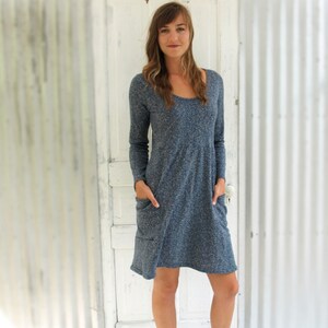 May include: A blue and grey long-sleeved dress with a scoop neck and pockets. The dress is being worn by a person with brown hair and is paired with brown lace-up boots.