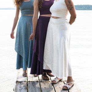 Puede incluir: Tres mujeres con faldas de envoltura de diferentes colores y tops sin mangas. Las faldas son todas largas y fluidas, y los tops son todos ajustados. Las mujeres est&aacute;n de pie en un muelle de madera, y el agua est&aacute; en el fondo.
