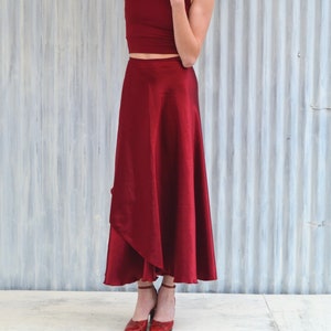 Puede incluir: Una mujer con un top rojo corto y una falda larga y fluida de color rojo. Est&aacute; de pie frente a una pared de metal corrugado plateado.