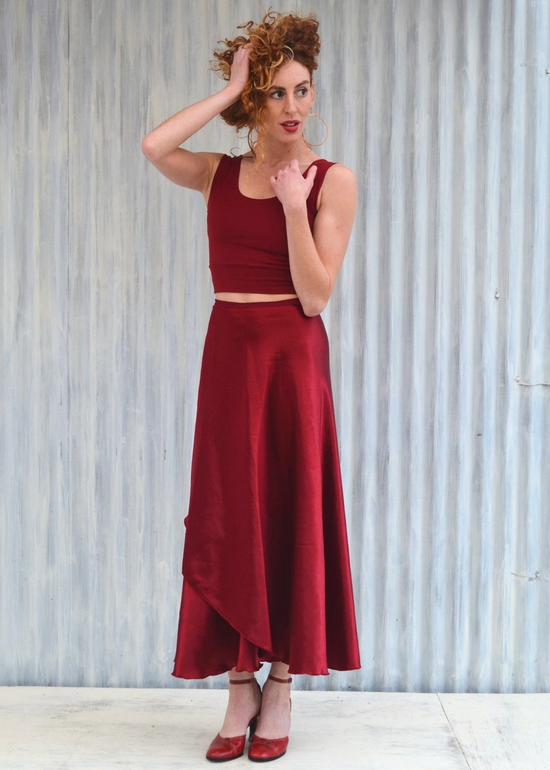 Puede incluir: Una mujer con un top rojo corto y una falda larga y fluida de color rojo. Est&aacute; de pie frente a una pared de metal corrugado plateado.