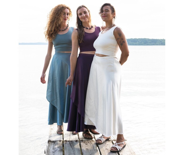 Puede incluir: Tres mujeres con faldas de envoltura de diferentes colores y tops sin mangas. Las faldas son todas largas y fluidas, y los tops son todos ajustados. Las mujeres est&aacute;n de pie en un muelle de madera, y el agua est&aacute; en el fondo.