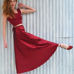 Puede incluir: Una mujer con un top rojo corto y una falda larga de sat&eacute;n rojo que se envuelve. Est&aacute; de pie con una pierna levantada y el pie apuntando, llevando tacones rojos.
