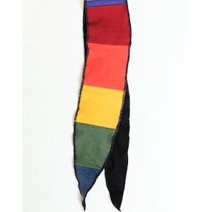 May include: A colorful scarf with a patchwork design. The scarf features rectangular blocks of color including blue, red, orange, yellow, green, and black. The scarf is made of a soft material and has a black border.