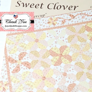 Puede incluir: Un patrón de acolchado para una colcha llamada "Sweet Clover" de Fig Tree Quilts. El patrón presenta un diseño floral con colores rosa, amarillo y blanco. El patrón es #FTQ 625.