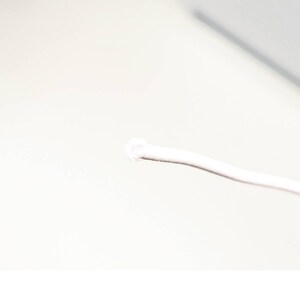 May include: A close-up of a white cord with a small white loop at the end. The cord is lying on a white surface.