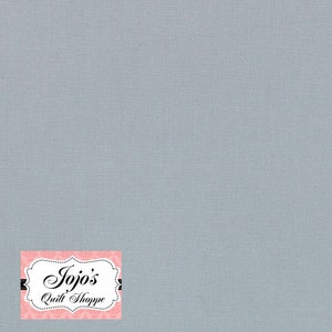 Puede incluir: Una tela azul claro sólida con una textura sutil. La tela tiene una etiqueta blanca con el texto "Jojo's Quilt Shoppe" en negro.