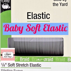 Puede incluir: Un paquete de trenza elástica suave de 0,3 cm. El paquete está etiquetado como "Baby Soft Elastic" y "Sold by the Yard". La marca "Dritz" es visible en la esquina superior izquierda. El paquete también incluye el texto "Elástico Suave".
