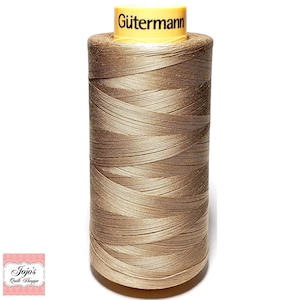 May include: A spool of Gütermann thread in a light brown color. The thread is tightly wound around the spool, with the brand name printed on the yellow top. The image is a close-up shot of the thread spool.