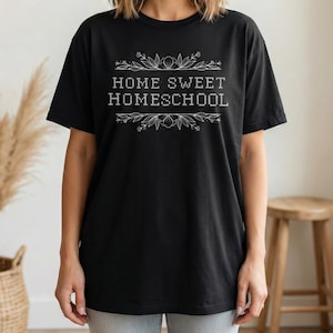 May include: Black t-shirt with the text "HOME SWEET HOMESCHOOL" in white, framed by floral and leaf designs. The shirt is a casual, everyday wear item.
