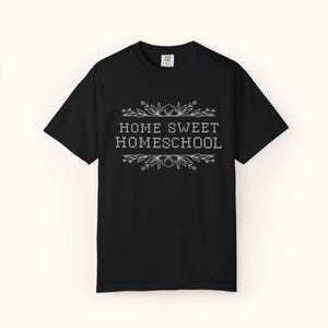 May include: Black t-shirt with the text "HOME SWEET HOMESCHOOL" in white, framed by floral and leaf designs. The shirt is a classic crew neck style.