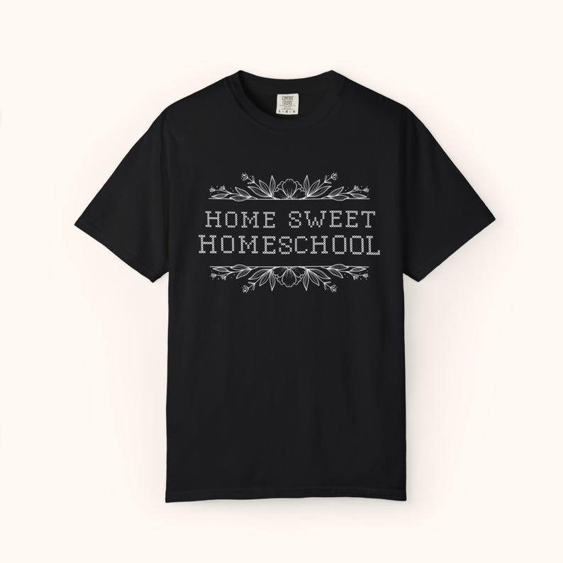 May include: Black t-shirt with the text "HOME SWEET HOMESCHOOL" in white, framed by floral and leaf designs. The shirt is a classic crew neck style.