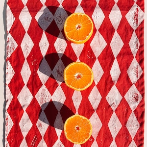 Puede incluir: Cuatro mitades de naranja dispuestas en línea vertical sobre un mantel de cuadros rojos y blancos.