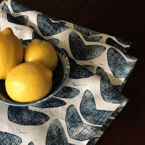Puede incluir: Tres limones amarillos en un tazón azul y blanco sobre una tela estampada azul y blanca con un fondo azul oscuro.