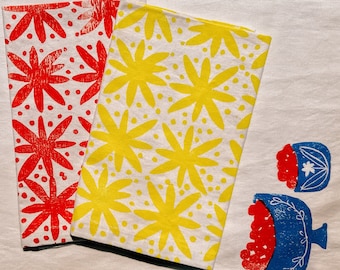 Pode incluir: Duas toalhas de cozinha com fundo branco e padrão floral. Uma toalha tem flores vermelhas e a outra tem flores amarelas.