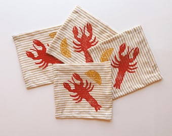 May include: Four beige and brown striped fabric napkins with red lobster and yellow lemon designs.