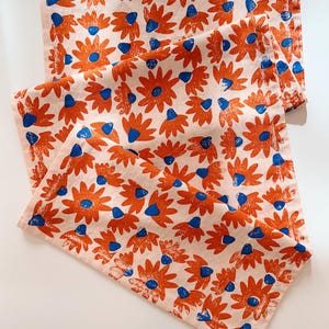 Puede incluir: Dos toallas de cocina con estampado floral naranja y azul, dobladas sobre una superficie blanca.