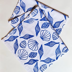 Może przedstawiać: Dwa białe bawełniane ręczniki kuchenne z niebieskim wzorem muszli. Ręczniki są złożone i ułożone jeden na drugim.