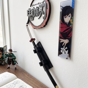 May include: A wall-mounted display featuring anime-themed decor. Includes a black and red circular emblem with Japanese text, a black sword with a white and red handle, and a character illustration. A figurine and sketchbook are also visible.