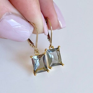 May include: A pair of gold earrings with square-shaped gray gemstones. The earrings have a simple, elegant design.