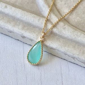 Puede incluir: Un delicado collar de cadena dorada con un colgante en forma de l&aacute;grima. El colgante est&aacute; hecho de vidrio azul claro con un borde dorado.