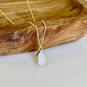 May include: A gold chain necklace with a white teardrop-shaped pendant made of druzy quartz.