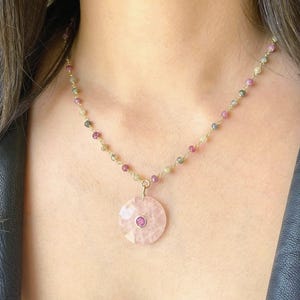 May include: A delicate gold necklace featuring a pink gemstone pendant with a smaller, round, pink gemstone center. The necklace chain is adorned with small, colorful beads in shades of pink, green, and yellow.
