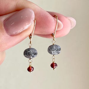 May include: Gold dangle earrings with a gray stone and a red gemstone.